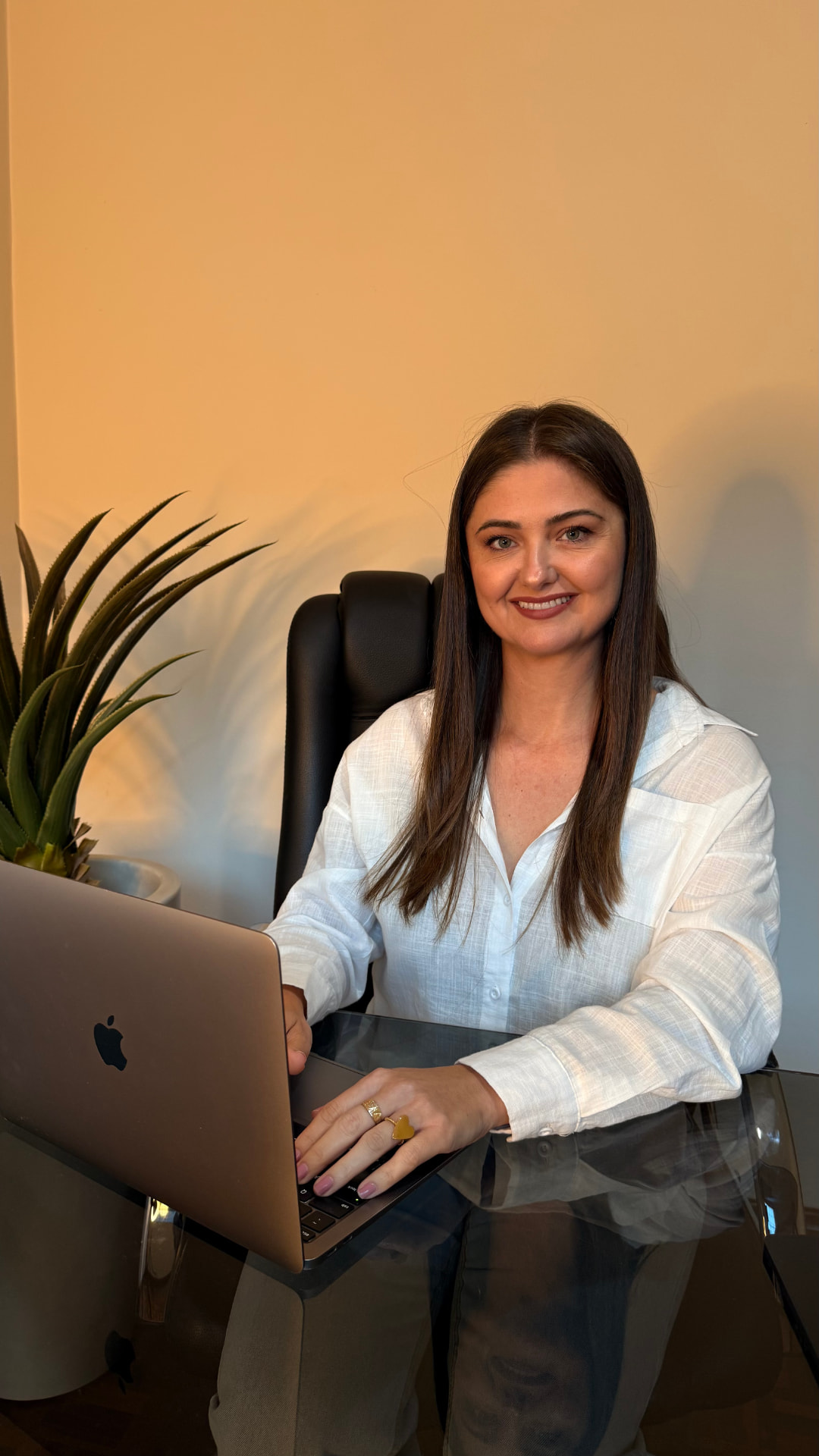 Lenisa Lucena sorrindo em sua mesa de atendimento, trabalhando no notebook